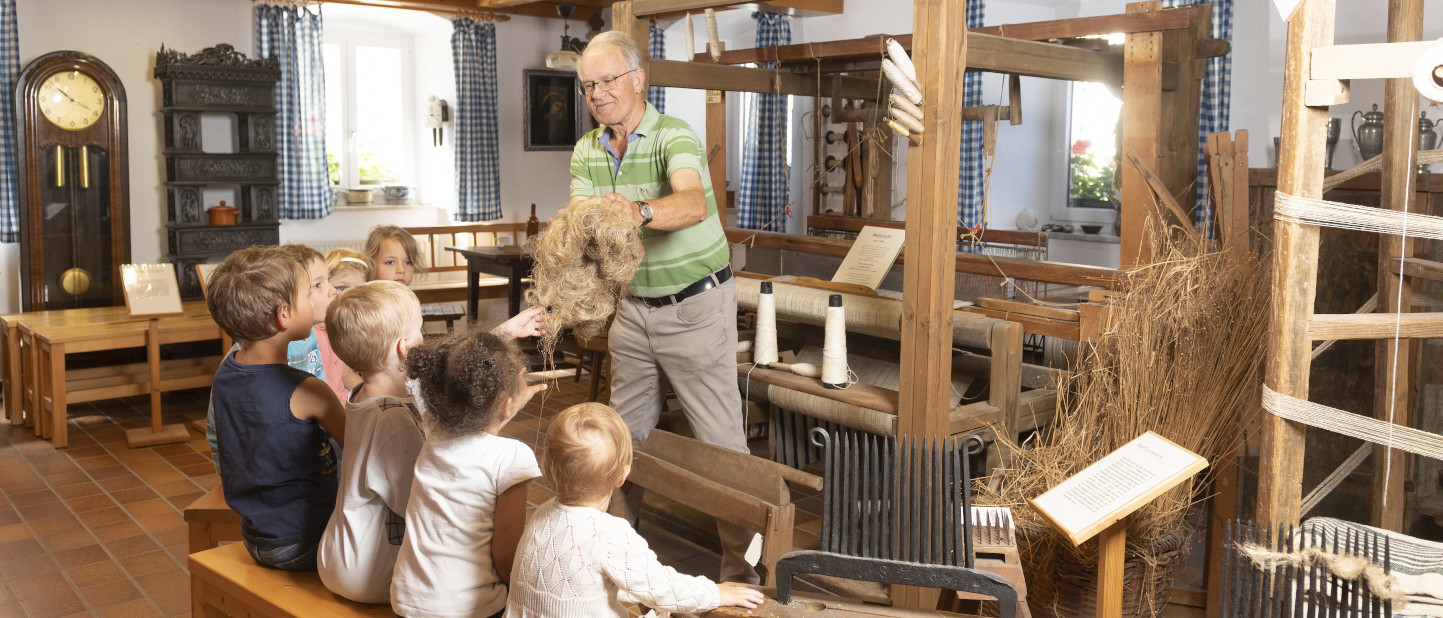 Mann zeigt Kindern Flachs in der Abteilung Weberei im Museum Erbendorf