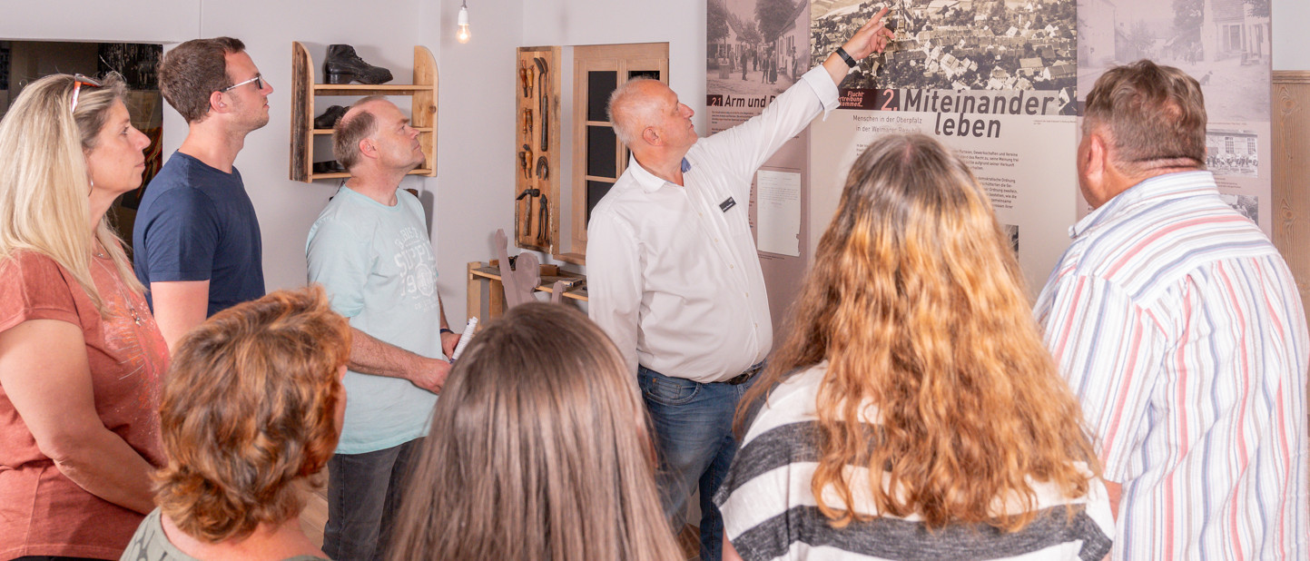 Sieben Personen sind bei einer Führung im Museum. Der Museumsführer zeigt ein Detail auf einer Karte.